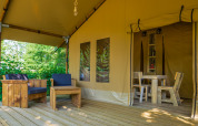 Terras van Slow Lodge safaritent met houten zithoek buiten en ingang tot de eettafel binnenin het tent.