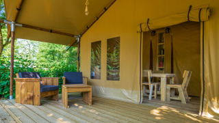 Deck of Slow Lodge safari tent featuring wooden outdoor seating and dining area entrance inside tent.