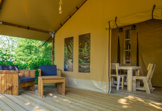 Terras van Slow Lodge safaritent met houten zithoek buiten en ingang tot de eettafel binnenin het tent.