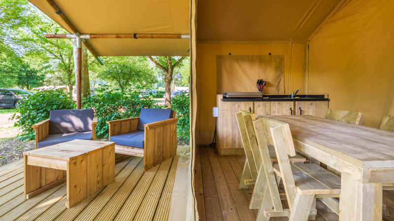 Safaritent bij Slow Lodge met houten meubilair, overdekt terras en ontspannen zithoek buiten.