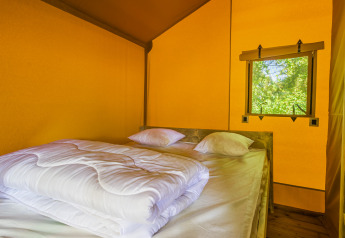 Interior de una tienda safari con cama doble, sábanas blancas y ventana con vistas al exterior natural.
