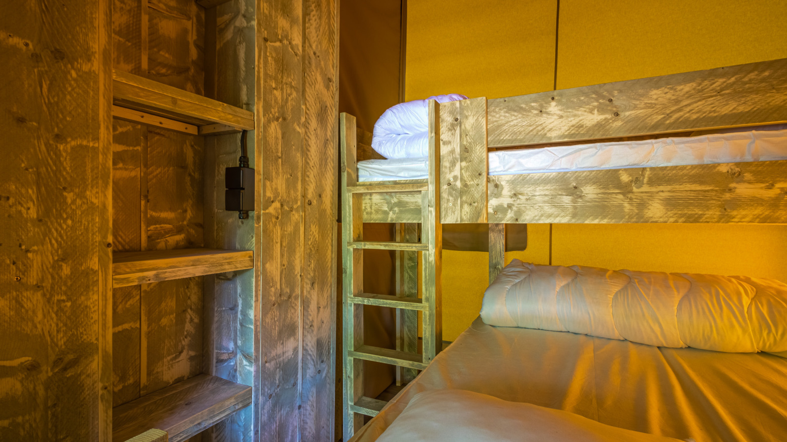 Interieur van de safaritent Slow Lodge met houten stapelbedden en planken in warm, sfeervol licht.