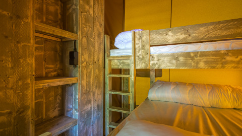 Interior de una tienda safari Slow Lodge con literas y estanterías de madera bajo luz cálida y acogedora.