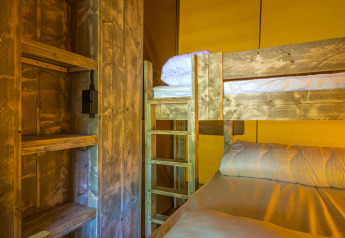 Interno della tenda safari Slow Lodge con letti a castello e scaffali in legno, illuminazione calda.