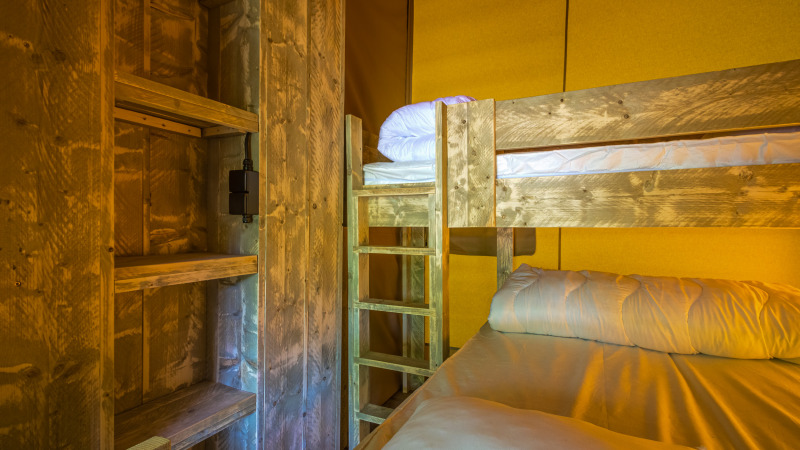 Interieur van de safaritent Slow Lodge met houten stapelbedden en planken in warm, sfeervol licht.