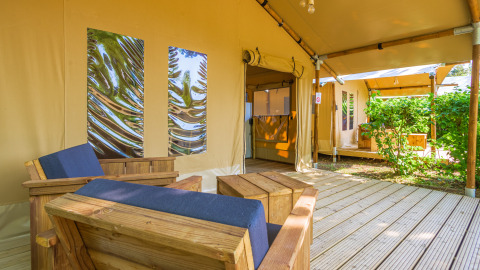 Acogedora zona de descanso en la tienda safari Slow Lodge con muebles de madera y vista al jardín.