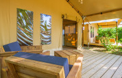 Acogedora zona de descanso en la tienda safari Slow Lodge con muebles de madera y vista al jardín.