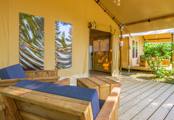 Gezellige zithoek in de safari tent Slow Lodge met houten stoelen en zicht op het groen buiten.