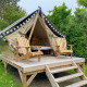 Glamping-telt på en hævet træplatform med to træstole foran og omgivet af grønne træer og buske.