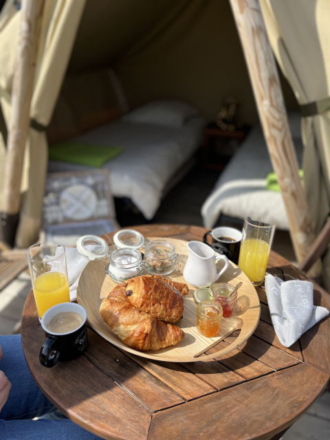 Breakfast with croissants, juice, and coffee on a small table outside a glamping tent with two beds.