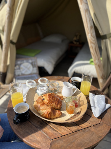 Frühstück mit Croissants, Saft und Kaffee auf einem kleinen Tisch vor einem Zelt mit zwei Betten.