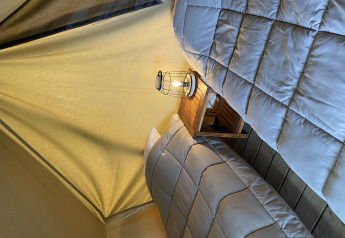 Dos camas individuales con edredones grises y una linterna sobre una mesita en una tienda de glamping.