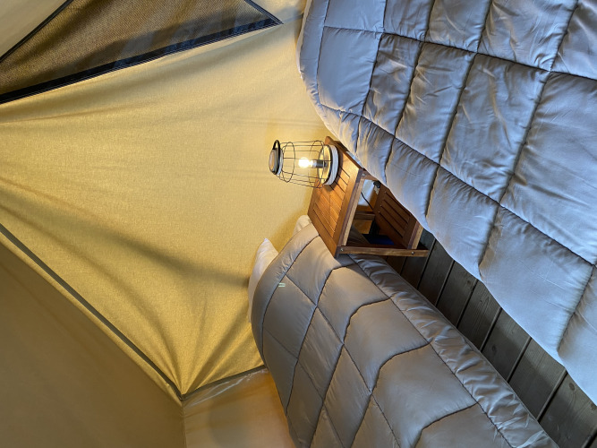 Twee eenpersoonsbedden met grijze dekbedden en een lantaarn op een nachtkastje in een glamping-tent.