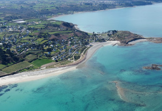 Luftfoto af Camping Seasonova Les 7 Iles i Bretagne, Frankrig, der viser kystlinje og feriepark.