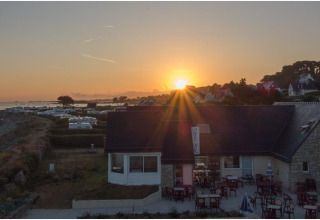 Tramonto sul Camping Seasonova Les 7 Iles, villaggio turistico sulla costa bretone in Francia, con tavoli all’aperto.