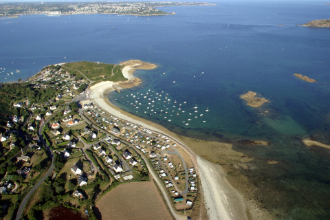 Vista aerea del Camping Seasonova Les 7 Iles in Bretagna, Francia, con spiaggia, case e barche sulla costa.