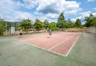 Vakantiegangers spelen tennis op het buitenveld van Camping Seasonova Les Vosges du Nord, Frankrijk.