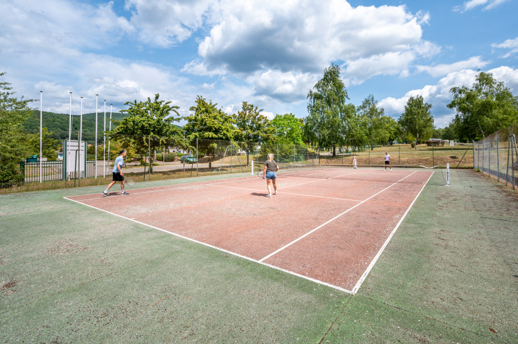 Gäste spielen Tennis auf dem Außenplatz des Camping Seasonova Les Vosges du Nord in Grand Est, Frankreich.