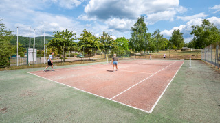 Huéspedes juegan al tenis en una pista exterior en Camping Seasonova Les Vosges du Nord, Grand Est, Francia.