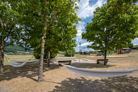 Camping al aire libre con hamacas entre árboles, bancos y parque infantil en Les Vosges du Nord, Francia.