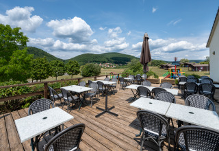 Terrazza esterna con tavoli e sedie al Camping Seasonova Les Vosges du Nord, Grand Est, Francia.