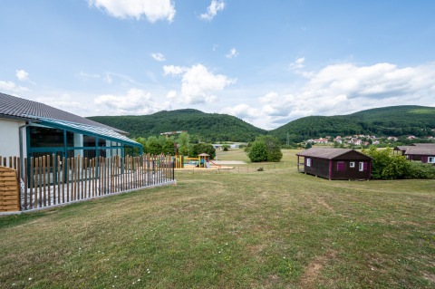 Vista de Camping Seasonova Les Vosges du Nord con colinas verdes, parque infantil y cabañas en Grand Est, Francia.