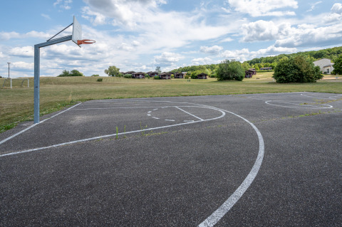 Campo da basket all'aperto con prato e bungalow al Camping Seasonova Les Vosges du Nord, Grand Est, Francia.
