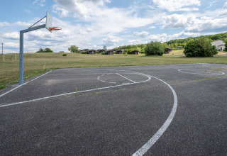 Campo da basket all'aperto con prato e bungalow al Camping Seasonova Les Vosges du Nord, Grand Est, Francia.