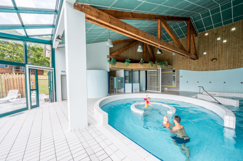 Piscina cubierta con familias y vigas de madera en Camping Seasonova Les Vosges du Nord en Grand Est, Francia.