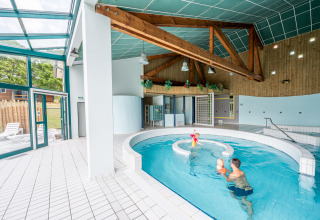 Binnenzwembad met gezinnen en houten balken bij Camping Seasonova Les Vosges du Nord in Grand Est, Frankrijk.