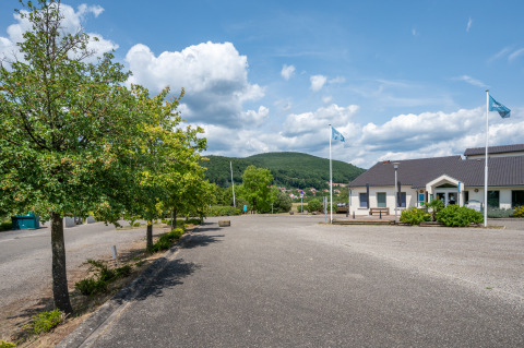 Holiday park in Grand Est, France, featuring a modern building, flags, trees, and green hills in the distance.