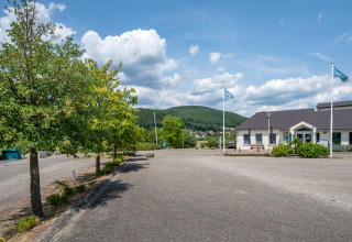 Holiday park in Grand Est, France, featuring a modern building, flags, trees, and green hills in the distance.
