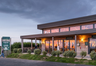 Avondzicht op vakantiepark Huttopia Les Falaises - Normandie, Frankrijk, gasten bij het café in warm licht.