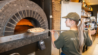 Un empleado horneando pizza en horno de piedra en Huttopia Les Falaises - Normandie, parque vacacional.