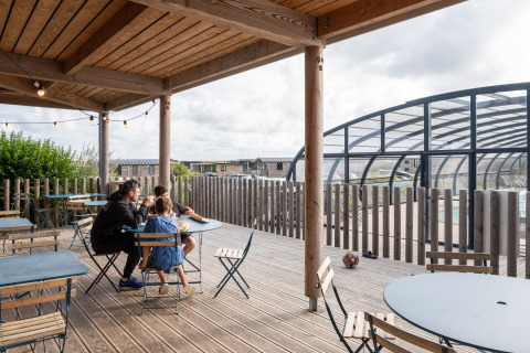 Gezin op het terras met zicht op het overdekt zwembad bij Huttopia Les Falaises, Normandië, Frankrijk.