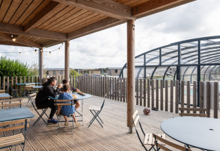 Gezin op het terras met zicht op het overdekt zwembad bij Huttopia Les Falaises, Normandië, Frankrijk.