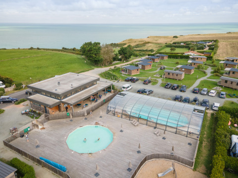 Vista aérea de Huttopia Les Falaises en Normandía, Francia, con cabañas, piscinas y vistas al mar.