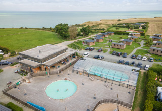 Luchtfoto van Huttopia Les Falaises in Normandië, Frankrijk, met chalets, zwembaden en zicht op zee.