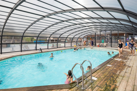 Piscine couverte avec baigneurs et terrasse en bois au village vacances Huttopia Les Falaises - Normandie, France.