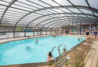 Overdekt zwembad met mensen en houten terras aan Huttopia Les Falaises - Normandie vakantiepark in Frankrijk.