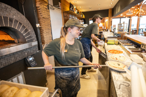 Zwei Pizzabäcker bereiten Pizzen an einem Holzofen im Huttopia Les Falaises – Normandie in Frankreich zu.