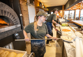 Twee pizzabakkers maken pizza's bij een steenoven in Huttopia Les Falaises - Normandie vakantiepark, Frankrijk.