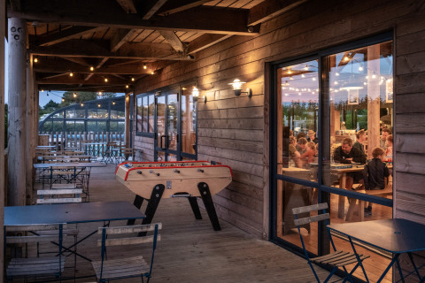 Evening view of a wooden terrace with foosball and seating at Huttopia Les Falaises holiday park in Normandy, France.