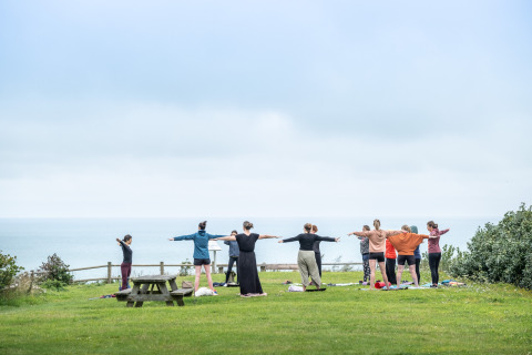 En gruppe mennesker laver udendørs yoga med udsigt over havet i Huttopia Les Falaises, Normandiet, Frankrig.