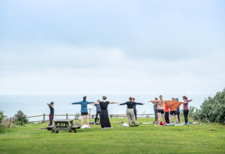 Un gruppo di persone pratica yoga all'aperto con vista mare a Huttopia Les Falaises, Normandia, Francia.