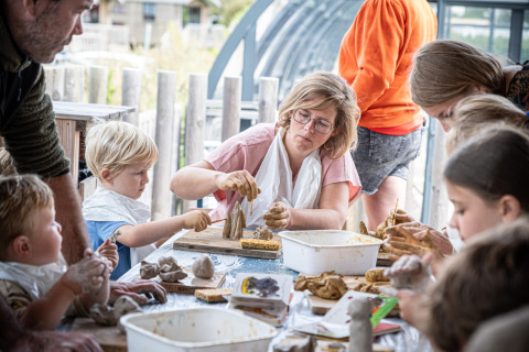 Niños y adultos crean figuras de arcilla juntos en una mesa en Huttopia Les Falaises - Normandie, Francia.