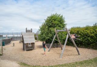 Speeltuin in Huttopia Les Falaises - Normandie, met spelende kinderen op schommels en houten speelhuisjes.