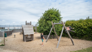 Parque infantil en Huttopia Les Falaises - Normandie, con niños en columpios y estructuras de madera al aire libre.