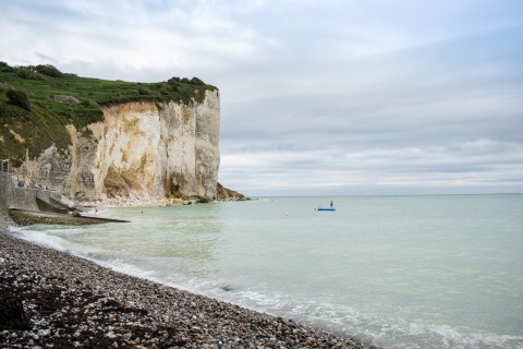 Coastal cliffs by Huttopia Les Falaises in Normandy, France, with pebble beach and calm sea under clouds.