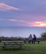 Dos personas sentadas en una mesa de picnic contemplan el atardecer cerca del mar en Saint-Pierre-en-Port, Normandía.